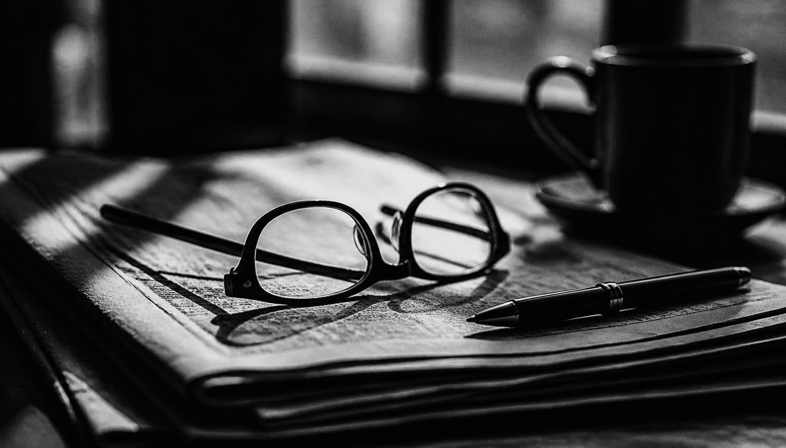 A newspaper and reading glasses on a dark desk